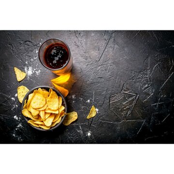 Beer with chips in a glass bowl. On black rustic background