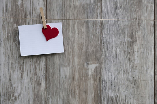Blank paper with red heart hanging on clothesline on wooden background