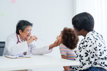 Gentle pediatrician examines a young girl's throat, as mother watches on with care in clinic....