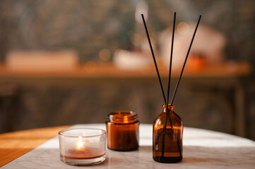 Liquid home perfume in dark brown glass bottle and bamboo sticks with burning candles on marble...