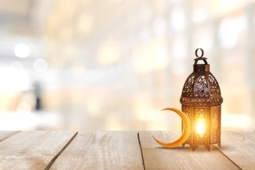 Rolgordijnen Ornamental Arabic lantern with burning candle glowing . Festive greeting card, invitation for Muslim holy month Ramadan Kareem. Ramadan Kareem greeting photo with serene mosque background.  © BHASKAR