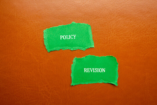 Policy revision lettering on green torn paper with brown background. Conceptual business symbol. Copy space.