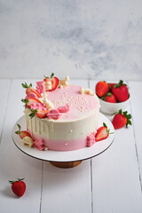 Delicious and beautiful handmade children's cake. Delicate pink and white cake for a child. Dessert is decorated with fresh strawberries and chocolate.