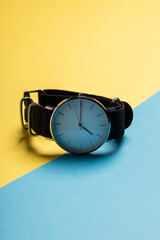 A hand watch with a white shield and tips lying on a yellow-blue background. Photo concept