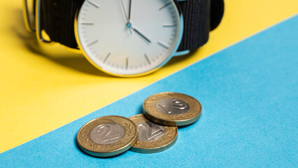 A hand watch with a white shield and tips lying on a yellow-blue background. Next to the Polish coins of PLN. Photo concept