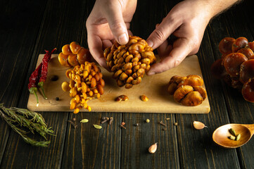Close-up of a man hands sorting stacks of flammulina mushrooms on the kitchen table before cooking.
