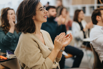 Enthusiastic woman clapping hands at workshop in casual business setting.