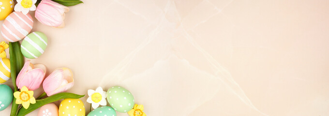 Easter eggs and flower decorations. Above view corner border against a soft pink stone banner background. Copy space.