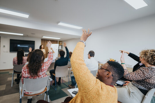 Diverse group of people actively participating in an educational workshop, raising their hands to ask questions or provide answers.