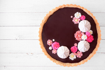 Gourmet chocolate tart with meringue and pink chocolate flowers. Top down view on a white wood background. Spring baking concept.