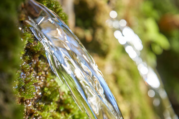 Crystal clear water jets flowing from moss covered wall.