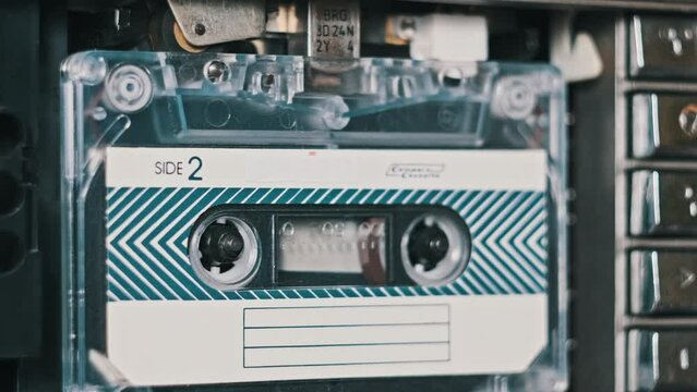 An audio cassette in a tape recorder is played in close-up. Playing audio cassette. Vintage record sound in a retro player. Recording or playback conversations. Retro tape reels rotate in deck. 80s