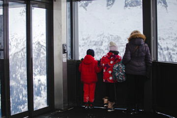 A family pauses to view the snow-covered mountains from a cable car station, sharing a moment of...