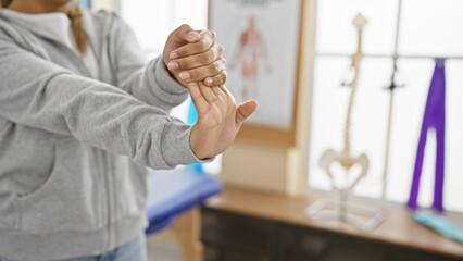 A young woman stretches her wrist in a bright rehabilitation clinic, indicating physical therapy...