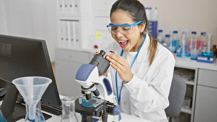 A surprised hispanic woman scientist examining a sample through a microscope in a laboratory setting.