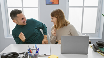Fototapeta premium A smiling man and woman engage playfully in a bright modern office, implying teamwork and positive workplace dynamics.
