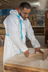 man in overalls inside carpentry shop working with machines and lifestyle, professional and industrial occupation, sanding wood to build handmade furniture