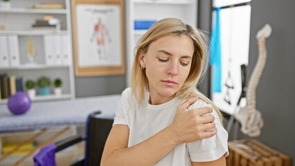 A young blonde woman showing discomfort in her shoulder at a modern physiotherapy clinic