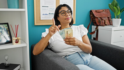 A confident woman gestures with brazilian currency in a modern office setting, exuding...