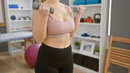 Fototapeta na wymiar Young woman exercising with dumbbells in a modern rehabilitation clinic setting.