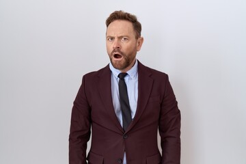 Middle age business man with beard wearing suit and tie in shock face, looking skeptical and sarcastic, surprised with open mouth
