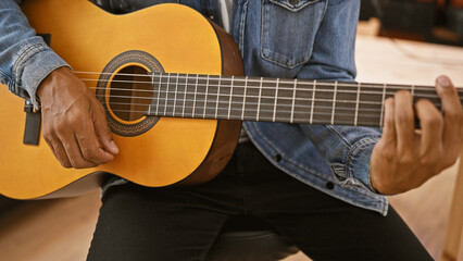 A young hispanic man casually plays guitar in an indoor music studio setting.