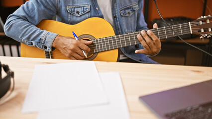 A young man composing music with a guitar in a studio setting, showcasing creativity and artistry.