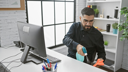 Bearded man cleaning office desktop with disinfectant spray and gloves