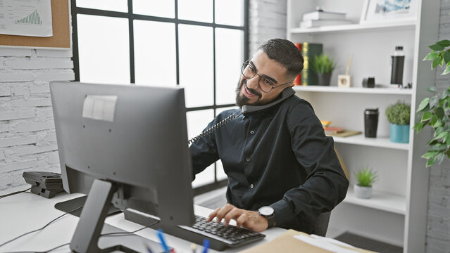 A smiling bearded man multitasking in a modern office setting, conveying professionalism and approachability.