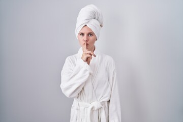 Blonde caucasian woman wearing bathrobe asking to be quiet with finger on lips. silence and secret concept.