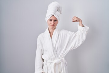 Blonde caucasian woman wearing bathrobe strong person showing arm muscle, confident and proud of...