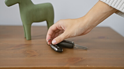 Close-up of a hand picking up car keys on a wooden table with a decorative object in a room.