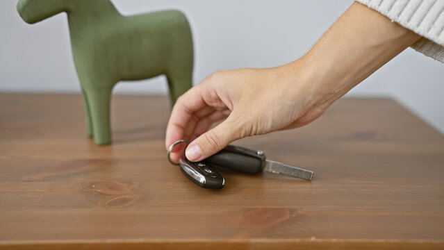 Close-up of a hand picking up car keys on a wooden table with a decorative object in a room.