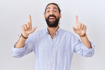 Fototapeta premium Hispanic man with beard wearing casual shirt smiling amazed and surprised and pointing up with fingers and raised arms.