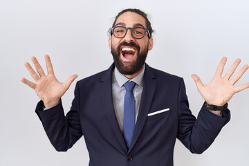 Hispanic man with beard wearing suit and tie celebrating crazy and amazed for success with arms raised and open eyes screaming excited. winner concept