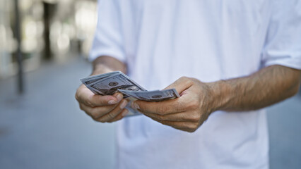 Casual hispanic man standing, his hands involved in the urban ritual, counting cash. dollars in...