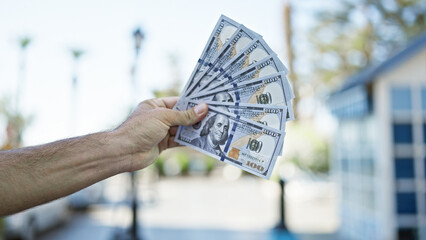 Hispanic man's hands casually holding dollar bills on a city street, a symbolic act of urban...