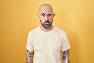 Hispanic man with tattoos standing over yellow background depressed and worry for distress, crying angry and afraid. sad expression.