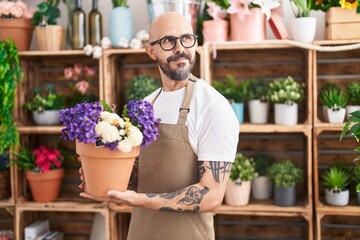 Young bald man florist smiling confident holding plant at florist