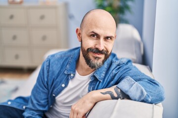 Fototapeta premium Young bald man smiling confident sitting on sofa at home