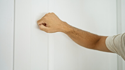 A close-up of a man's clenched fist knocking on a white door, emphasizing anticipation and arrival...