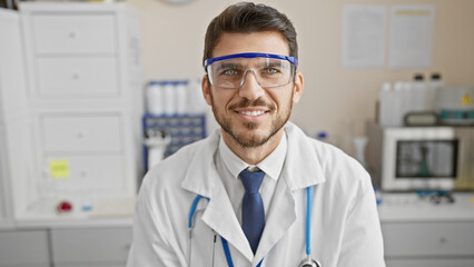 Hispanic man in lab with goggles, stethoscope, tie, white coat, indoors, smiling, professional,...