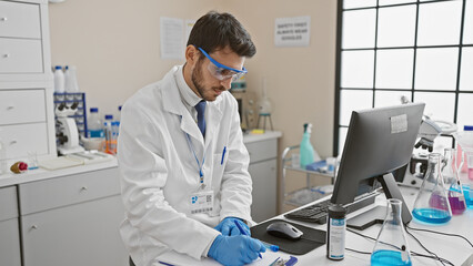 Focused young man in a laboratory setting inspecting information on the computer amidst lab...