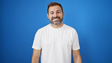A smiling hispanic mature man with grey hair poses against a vibrant blue background outdoors.