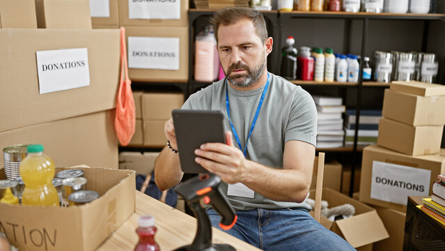 Mature hispanic man holding tablet in a donation center with boxes labeled 'donations' in the background