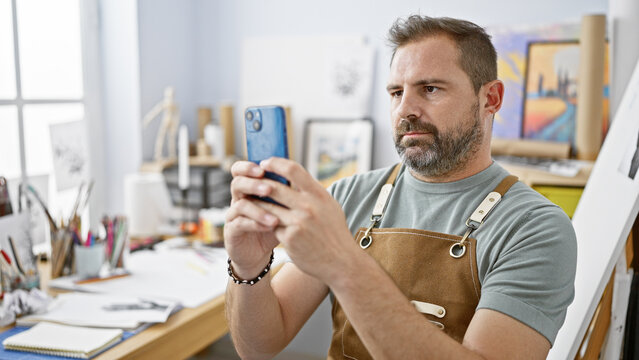 Handsome mature man with grey hair taking a selfie in an art studio setting.