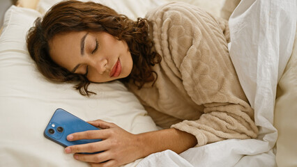 A woman sleeps in a bed holding a smartphone, suggesting a connection to technology even in restful moments.