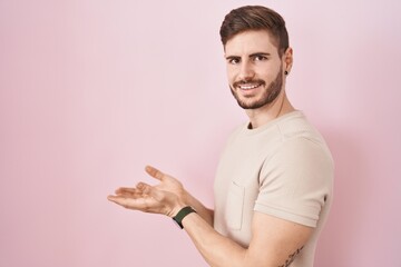 Hispanic man with beard standing over pink background pointing aside with hands open palms showing copy space, presenting advertisement smiling excited happy