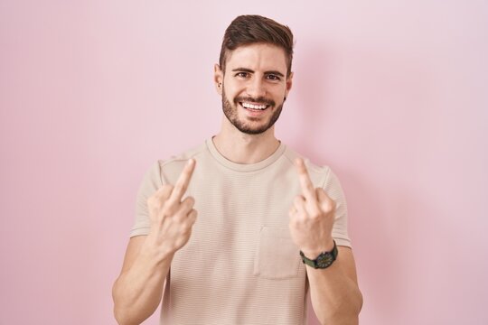 Hispanic man with beard standing over pink background showing middle finger doing fuck you bad expression, provocation and rude attitude. screaming excited