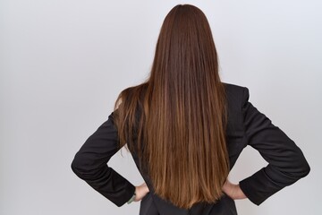 Beautiful brunette woman wearing business jacket and glasses standing backwards looking away with arms on body